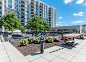 Thumbnail 19 of 21 - A modern outdoor seating area with benches and a fountain in front of apartment buildings.