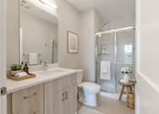 Thumbnail 7 of 22 - Modern apartment bathroom at Creekline at Fairfield in Fairfield, CT with quartz-style vanity, light wood cabinetry, large mirror, and sliding glass shower with marble-look tile.