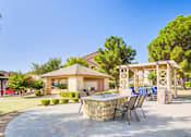 Thumbnail 17 of 20 - A patio with a barbecue grill and chairs is surrounded by a stone wall and trees.