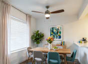 Thumbnail 6 of 35 - Pet-Friendly Apartments in Everett, WA - Woodbrook - Dining Area With A Wooden Table, Upholstered Chairs, Large Window, Colorful Wall Art, And Kitchen Breakfast Bar.