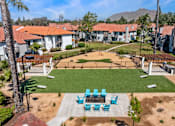 Thumbnail 8 of 28 - One Bedroom Apartments In Moreno Valley, CA - Ardella On Chagall - An Aerial View Of A Community Dog Park With A Bone-Shaped Turf Area, Adjacent To A Fire Pit And Lawn Games.