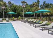 Thumbnail 16 of 35 - Savannah, GA Apartments – The Palms at Chatham– a pool with chaise lounge chairs and umbrellas