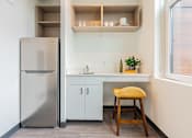 Thumbnail 22 of 54 - A small kitchen with a refrigerator, a sink, and a stool.