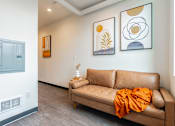 Thumbnail 27 of 54 - A tan couch with an orange throw sits in a room with two framed pictures on the wall.