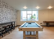 Thumbnail 37 of 54 - A pool table in a room with a bar and a window.