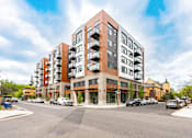 Thumbnail 52 of 54 - A modern apartment building with a parking lot in front.
