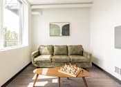 Thumbnail 5 of 54 - A room with a green couch, a wooden coffee table with a chess board on it, and a painting on the wall.