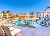 Thumbnail 14 of 29 - A pool surrounded by chairs and buildings.