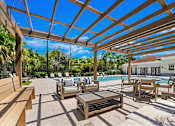 Thumbnail 13 of 15 - A wooden pergola over a poolside seating area.