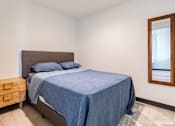 Thumbnail 10 of 40 - A bedroom with a bed, nightstand, and a mirror.