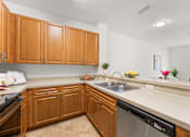 Thumbnail 7 of 15 - Pet-Friendly Townhomes in Kissimmee, FL – Estates at Lake Cecile -A kitchen with wooden cabinets and a stainless steel dishwasher.