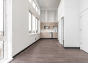 Thumbnail 24 of 40 - A long, empty room with a kitchen area in the background.