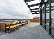 Thumbnail 36 of 40 - A rooftop patio with benches and a glass wall overlooking the city.
