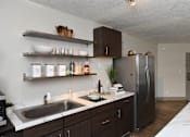 Thumbnail 3 of 51 - A kitchen with a sink, refrigerator, and shelves with various items.
