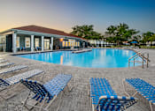 Thumbnail 12 of 28 - A poolside area with blue lounge chairs and a building in the background.
