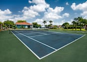 Thumbnail 13 of 28 - A tennis court with a blue sky and clouds in the background.