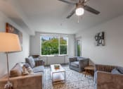 Thumbnail 1 of 28 - Apartments in Fremont, WA for Rent - Epicenter - Furnished Living Room with Ceiling Fan, Large Window, and Patio/Balcony Access