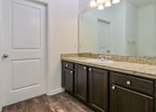 Thumbnail 57 of 75 - A bathroom with a white door, brown cabinets, and a marble countertop.