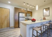 Thumbnail 1 of 20 - South Seattle, WA, Pet-Friendly Apartments - Greenhouse - Contemporary Kitchen with Karndean Wood Flooring, Energy Star Silver Metallic Appliances, Wood-Tone Cabinets, Stylish Granite Countertops, Breakfast Bar with Bar-Style Chairs, and Pendant Lights.