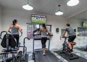 Thumbnail 21 of 35 - A gym with people exercising and a TV screen showing a soccer game.