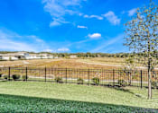 Thumbnail 47 of 63 - A black fence surrounds a green lawn with a tree and a house in the distance.