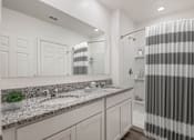 Thumbnail 28 of 35 - A bathroom with a striped shower curtain and a marble countertop.