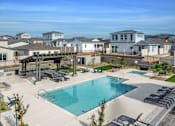 Thumbnail 22 of 47 - A large swimming pool surrounded by a patio with lounge chairs and a pavilion.