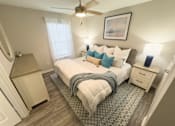 Thumbnail 12 of 29 - Twin Oaks Apartments in Hattiesburg Mississippi A bedroom with a large bed, a ceiling fan, and a window with white curtains.