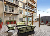 Thumbnail 17 of 20 - A patio area with a black wicker sofa and a table with a yellow cushion.