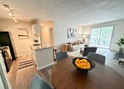 Thumbnail 3 of 35 - A kitchen area with a refrigerator, a dining table with chairs, and a bowl of oranges on the table.