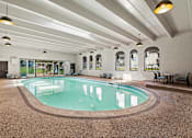 Thumbnail 2 of 42 - A large indoor swimming pool with a brown floor and white walls.