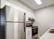 Thumbnail 13 of 42 - Aurora, CO Apartments – Ivy Crossing – A kitchen with a fridge, white cabinets, and a stove top oven.