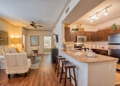 Thumbnail 17 of 33 - Living room with wood floors and couches and chairs and windows with blinds and ceiling light and kitchen with chairs