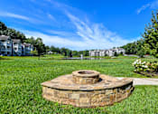 Thumbnail 10 of 17 - A stone fire pit sits in the middle of a grassy area.