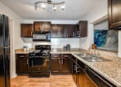 Thumbnail 14 of 17 - A kitchen with a black refrigerator and brown cabinets.
