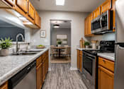 Thumbnail 1 of 25 - Modern apartment kitchen at Lancaster Place Apartments in Calera, Alabama with stainless-steel appliances, wood cabinetry, generous counter space, and ample storage.