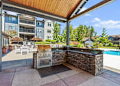 Thumbnail 15 of 18 - A patio with a stone wall and a grill is shown.
