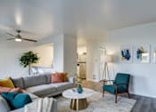 Thumbnail 4 of 35 - Dog-Friendly Apartments in Everett, WA - Woodbrook - Living Room With A Gray Sectional Sofa, Colorful Accent Pillows, Teal Chair, Round Coffee Table, and Wall Art.