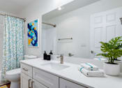 Thumbnail 9 of 35 - 2-Bedroom Apartments in Everett, Washington - Woodbrook - Bathroom With A White Vanity, Large Mirror, Bathtub, Colorful Wall Art, Folded Towels, And Green Plant.