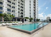 Thumbnail 5 of 19 - Miami, FL Apartments - MB Station - Apartment Balconies Overlooking Sparkling Resort-Style Pool Surrounded by Lounge Seating and Umbrellas