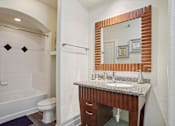 Thumbnail 12 of 22 - Apartments for Rent in North Little Rock, AR 72114– Metropolitan-   A bathroom with a white tub and a wooden vanity.