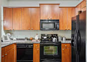 Thumbnail 4 of 22 - 1, 2 -Bedroom Apartments for Rent in North Little Rock, AR – Metropolitan– A kitchen with black appliances and wooden cabinets.