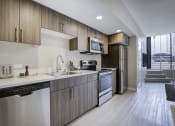 Thumbnail 29 of 36 - Modern Studio Apartments in Seattle, WA - Origin - Kitchen with Contemporary Wood-Finish Flooring, Stainless Steel Appliances, Stone Countertops, and Wood-Tone Cabinets
