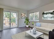 Thumbnail 2 of 17 - Coeur d' Alene, ID, Apartments For Rent - Living Room With Upgraded Wood-Style Flooring. Area Rug, Couch, Armchairs, Coffee Table, Wall Art, Houseplant, Window, And Sliding Glass Door With Balcony Access.