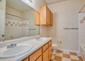 Thumbnail 12 of 20 - Apartments In Beaumont, TX for Rent – Breakwater Bay - Bathroom with tile flooring, double vanity, cabinets below sink, giant mirror above sink, toilet with storage above, and tub/shower