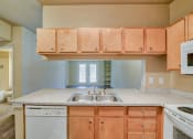Thumbnail 4 of 24 - A living room and kitchen with wood flooring and wood cabinets with white dishwasher and white microwave and stove top with oven and steel sink
