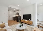 Thumbnail 18 of 78 - Modern open-plan living space with hardwood flooring, featuring a cozy sitting area with a white round marble-top coffee table, sleek TV stand, and an understairs white door.