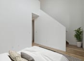 Thumbnail 46 of 78 - Minimalist bedroom featuring a double bed with light bedding, abstract artwork, and a stairway leading to an upper level, creating a sense of space and simplicity.