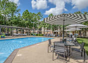 Thumbnail 20 of 39 - Apartments In Houston Texas for Rent – Westchase Forest - Photo of a swimming pool with tables and umbrellas next to it