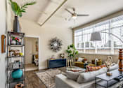 Thumbnail 15 of 39 - A living room with a large window, a sofa, a coffee table, and a plant on a shelf.